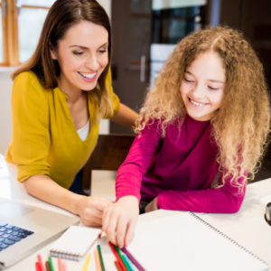 Enseignante accompagnant une élève sur un exercice écrit, à la table de la maison
