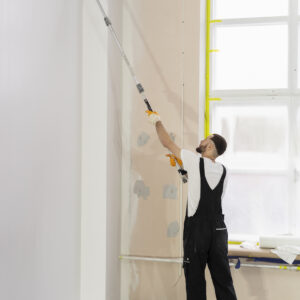 Peintre appliquant la peinture au rouleau à manche télescopique sur un mur d’intérieur