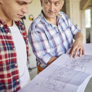 Deux artisans examinant un plan d’architecte déplié sur un chantier de rénovation