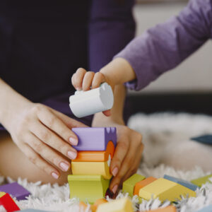 Une adulte et un jeune enfant empilent ensemble des cubes en bois colorés sur un tapis
